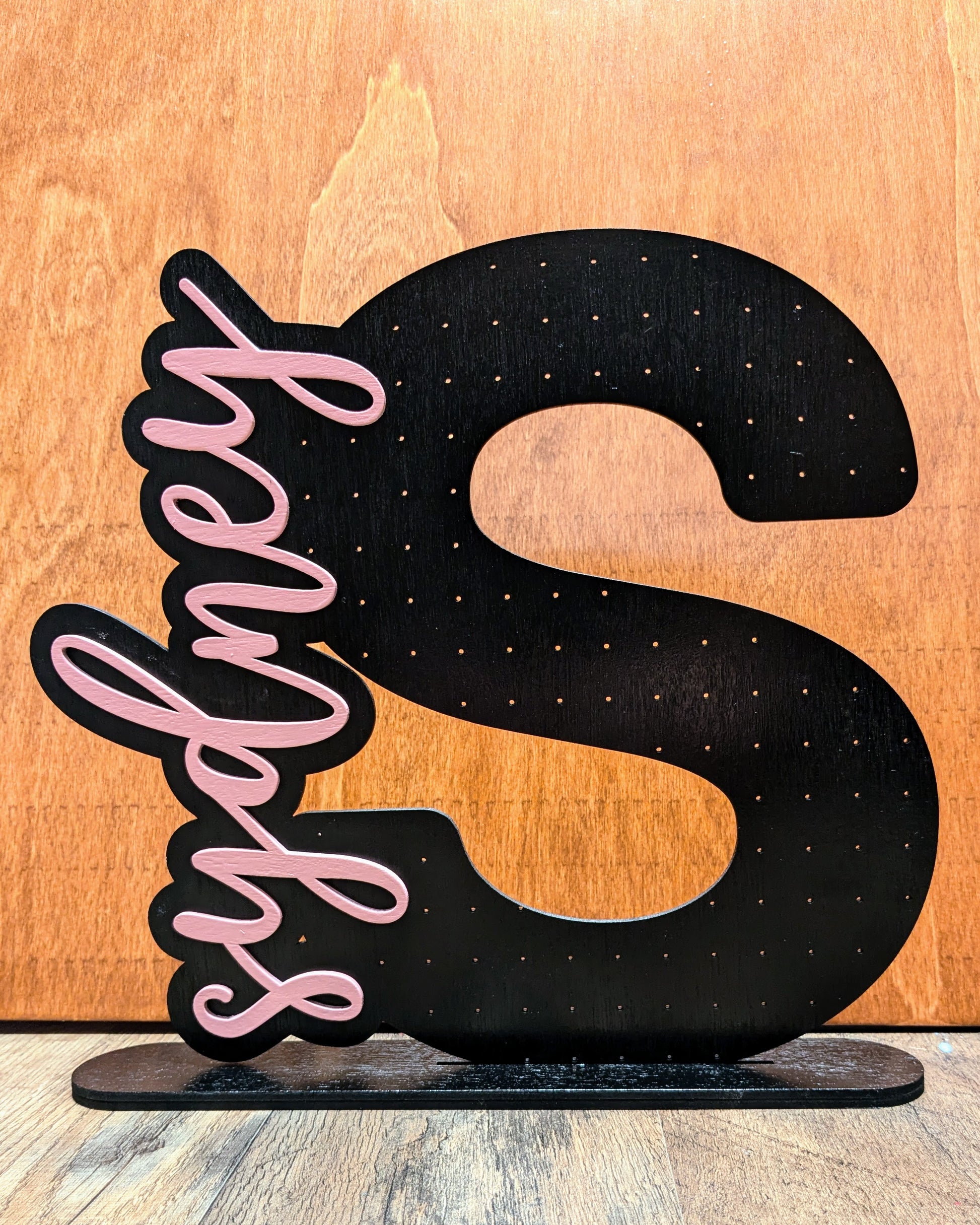 a wooden sign with a black and pink letter s